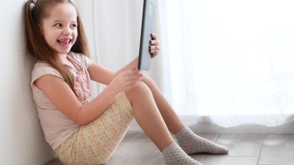 Baby Little Girl Holding and Using Pc Tablet and Sits on the Floor in Room