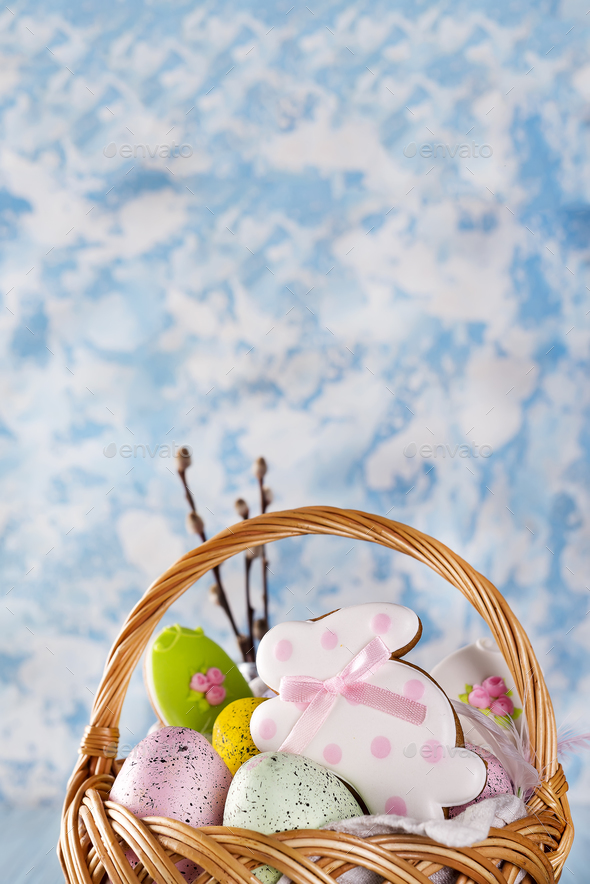 Easter cookies, bunnies and Multicolored Easter eggs in a basket on light blue background - Stock Photo - Images
