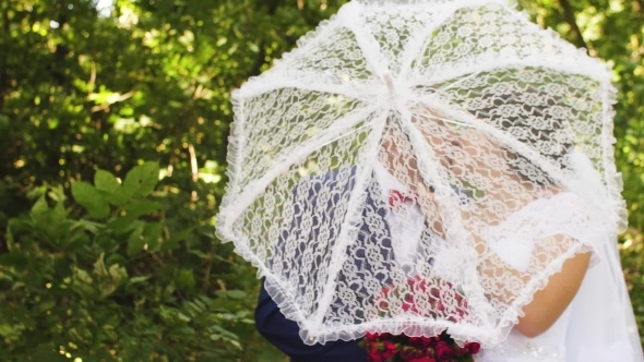 Bride and Groom Walking in Park with a White Umbrella on Romantic Wedding