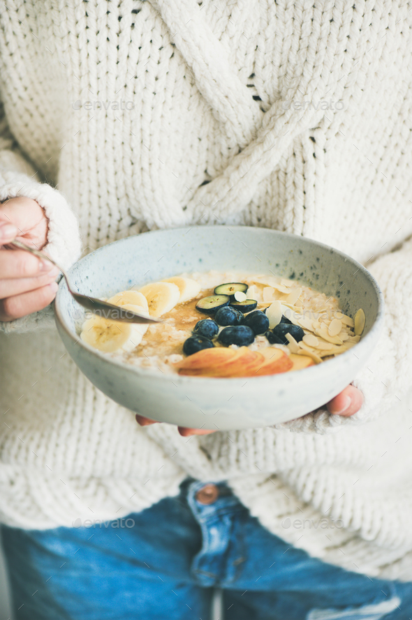 Woman in jeans and sweater eating oatmeal porriage - Stock Photo - Images