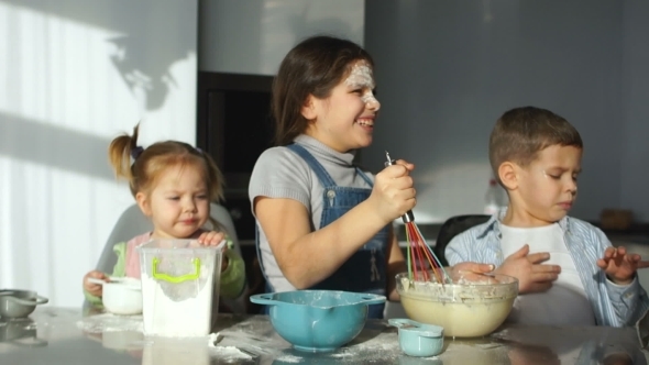 Three Children Prepare Dough in the Kitchen. The Elder Sister Helps His Brother To Stir the Dough alt