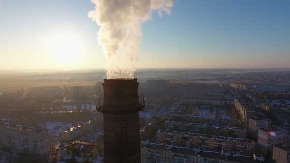 Aerial Shot of High Industrial Tube with White Smoke in Snowy City at Sunset in Winter