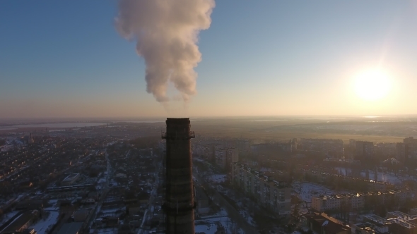 Aerial Shot of Immense Chimney with White Smoke in Snowy City at Sunset in Winter