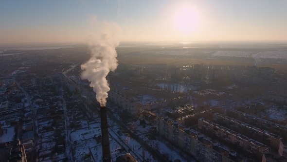 Aerial Shot of Huge Flue Tower with White Smoke in Snowy City at Sunset in Winter