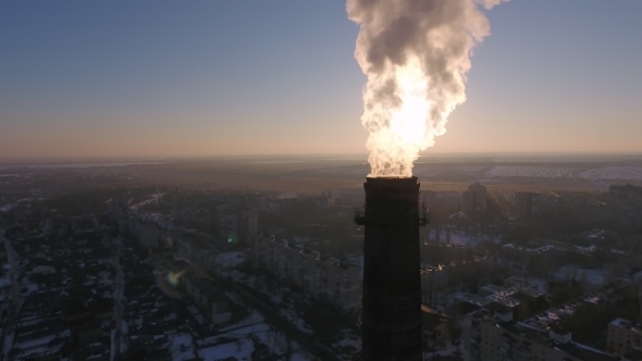 Aerial Shot of High Tube with White Flame Looking Smoke in Snowy City at Sunset