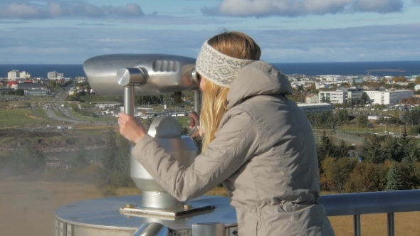 Young Tourist Girl Is Looking in a Stationary Telescope on Reykjavik in Sunny Day