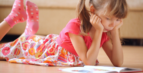 Little Girl Reads Book Lying on the Floor