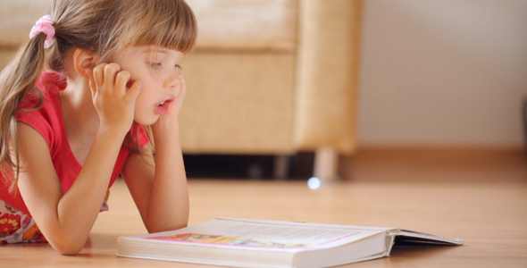 Little Girl Reads Book Lying on the Floor