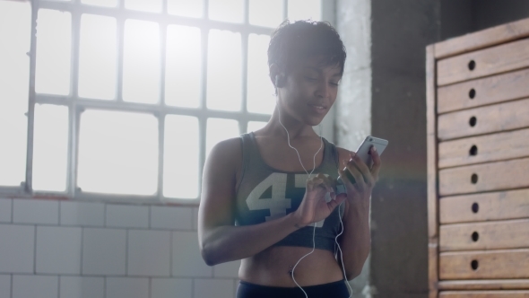 Young Fit and Tone Up Woman Doing Fitness Workoutand Choosing a Song in Smartphone alt