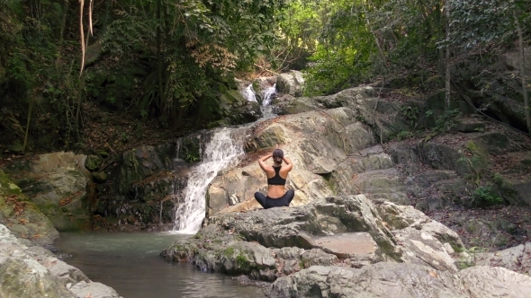 Young Woman Meditates at the Waterfall