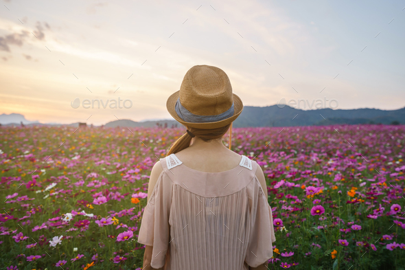 Young woman traveler looking beautiful flowers field - Stock Photo - Images