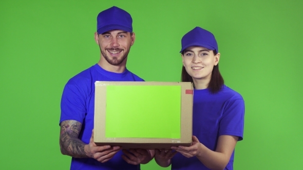 Two Happy Professional Delivery Workers Holding Out Package Box To the Camera alt