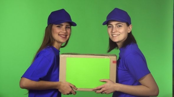 Two Cheerful Female Delivery Service Workers Smiling Holding Cardboard Box alt
