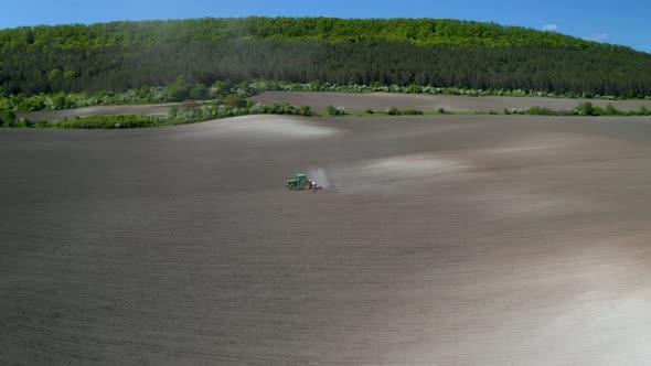 Field with picturesque hills and a moving tractor alt
