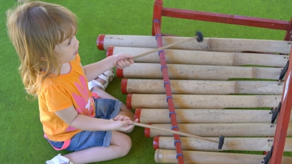 Little Girl Plays with Special Sticks on Traditional Indonesian Instruments alt