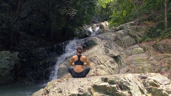 Young Woman Meditates at the Waterfall