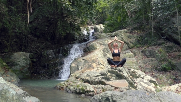 Young Woman Meditates at the Waterfall