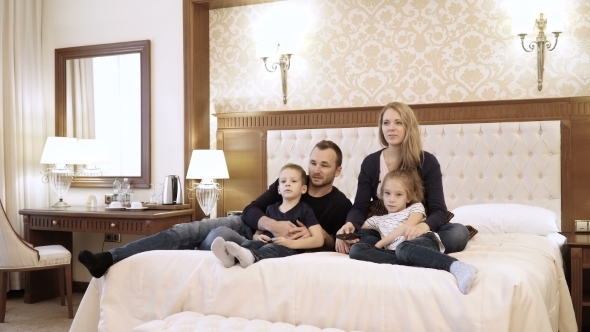 a Happy Family Watching Television in Hotel Room Sitting on Bed