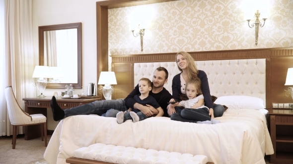 a Happy Family Watching Television in Hotel Room Sitting on Bed