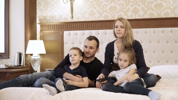 a Happy Family Watching Television in Hotel Room Sitting on Bed