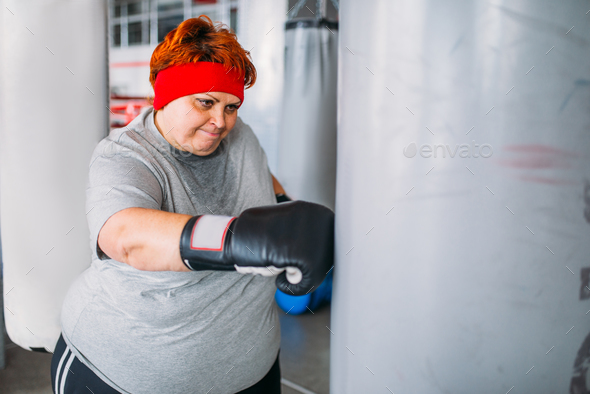 Fat woman in boxing gloves works with punching bag - Stock Photo - Images