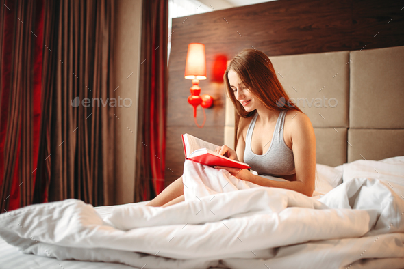 Beautiful woman in underwear reads the book in bed - Stock Photo - Images