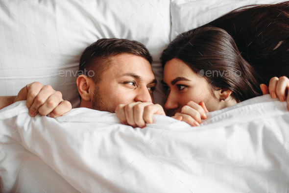 Shy love couple lies on big white bed, top view - Stock Photo - Images