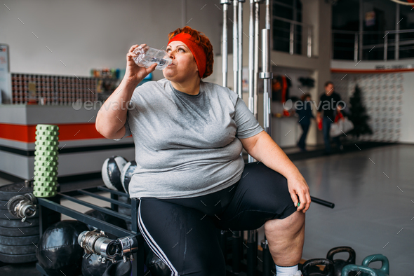 Fat woman drinks water after training in gym - Stock Photo - Images
