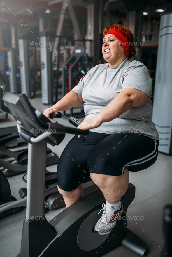 Fat woman training on exercise bike in gym - Stock Photo - Images
