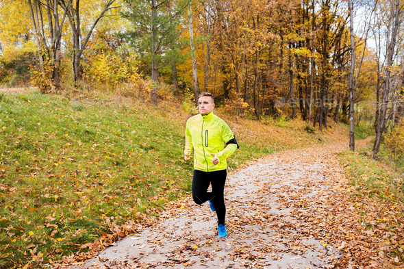 Young athlete with smartphone running in park in autumn. - Stock Photo - Images