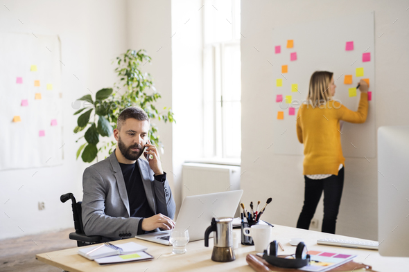 Two business people with wheelchair in the office. - Stock Photo - Images