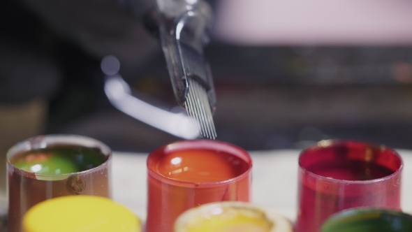 Artist Dunks Tattoo Machine in Orange Paint. . Mixing Colors. Master Dipping the Gun Needle Into alt