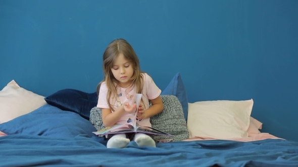 A Little Girl Is Reading a Book on the Bed alt