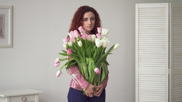 Young Middle Eastern Woman with Sad Eyes Holding Flowers in Hands at Home