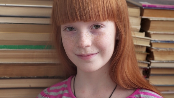 of a Little Happy School Girl Smiling on Background of Books