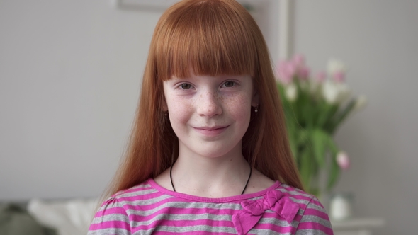 Little Red-haired Girl with Freckles Smiling in a White Room