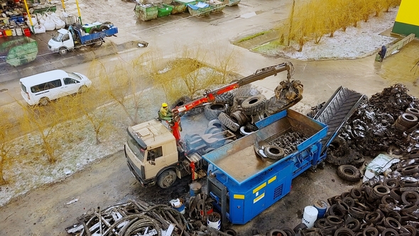 Waste Recycling Plant. The Truck Crane Loads Old Tires Into the Shredder for Recycling alt