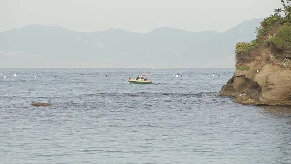 a Small Boat Sailing Along the Sea, on the Background of an Island with Mountains