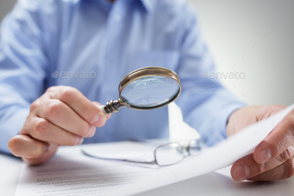 Businessman with magnifying glass reading documents Stock Photo by