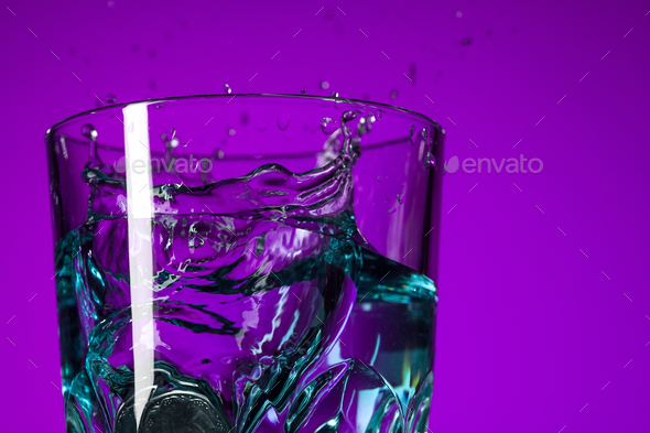 The water splashing in glass on lilac background - Stock Photo - Images