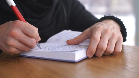 a Male Freelancer Writes a Note in a Notebook on a Wooden Table