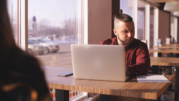 Young Bearded Businessman Sits in Cafe at Table. On Table Laptop. Man Is Working, Studying. Online