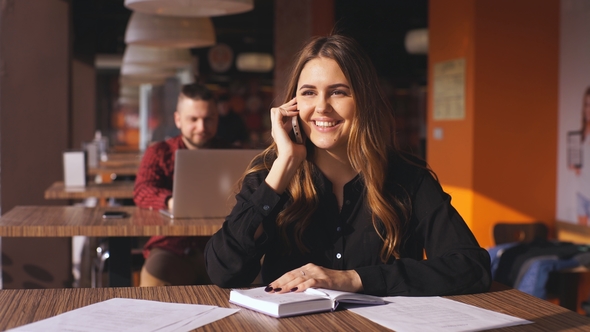 Cheerful Young Beautiful Woman Sitting in a Cafe and Talking on the Phone