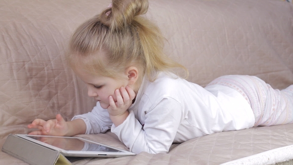 Cute Young Girl Lying on Sofa and Using a Digital Tablet.