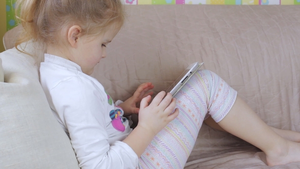 Cute Young Girl with Tablet at Home. Girl Using a Tablet Lying on the Sofa