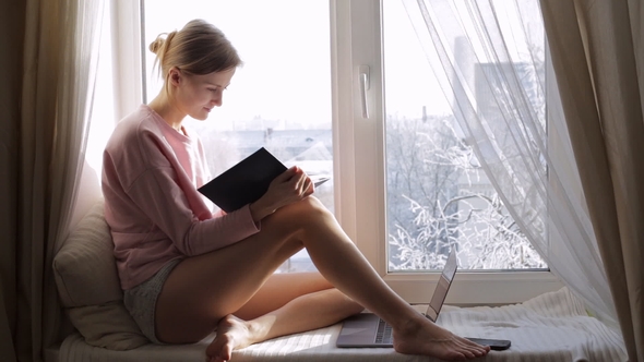 Dreaming Young Girl Read Book Sitting at Window Sill at Home. Winter Outside