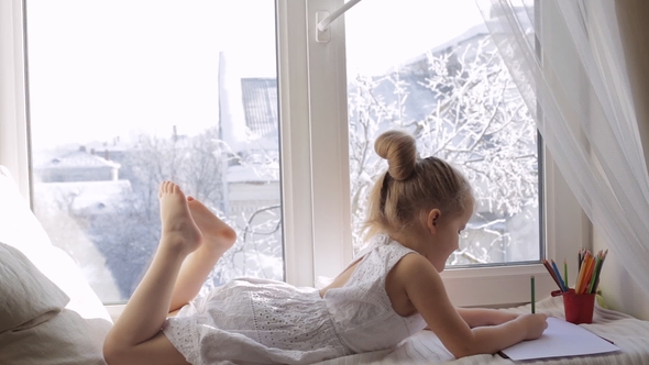 Cute Little Child Girl Draws with Colorful Pencils. Girl Lies on the Window Sill