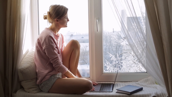 Cute Woman Using Her Laptop Sitting on Window Sill