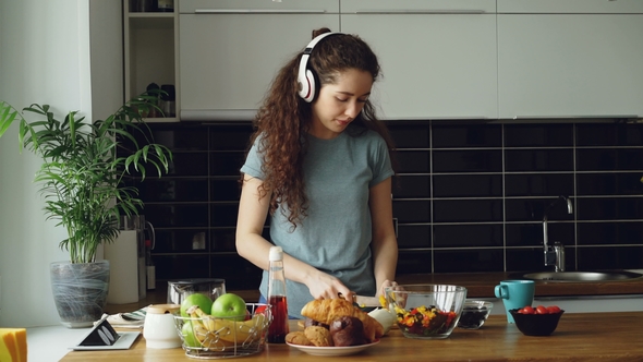 Attractive Happy Girl in Headphones Dancing and and Listening To Music While Cooking Healthy alt