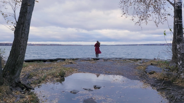Rear View of a Girl with Flowing Red Hair Dressed in Red Coat Against the Backdrop of a Lake and alt